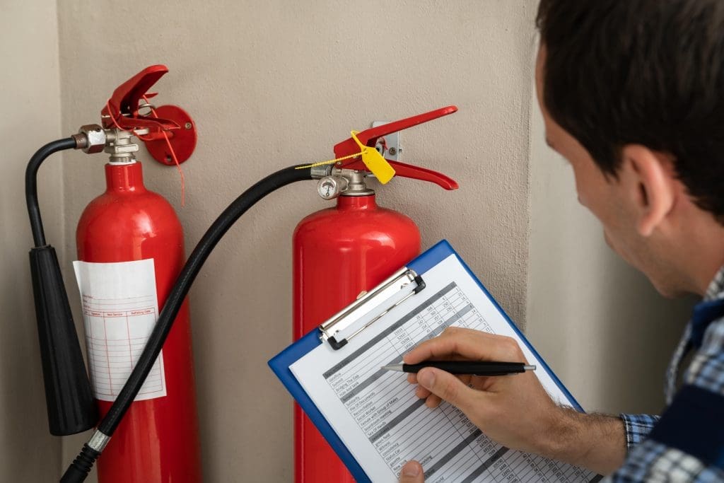 a man with a clipboard closely examines two fire extinguishers
