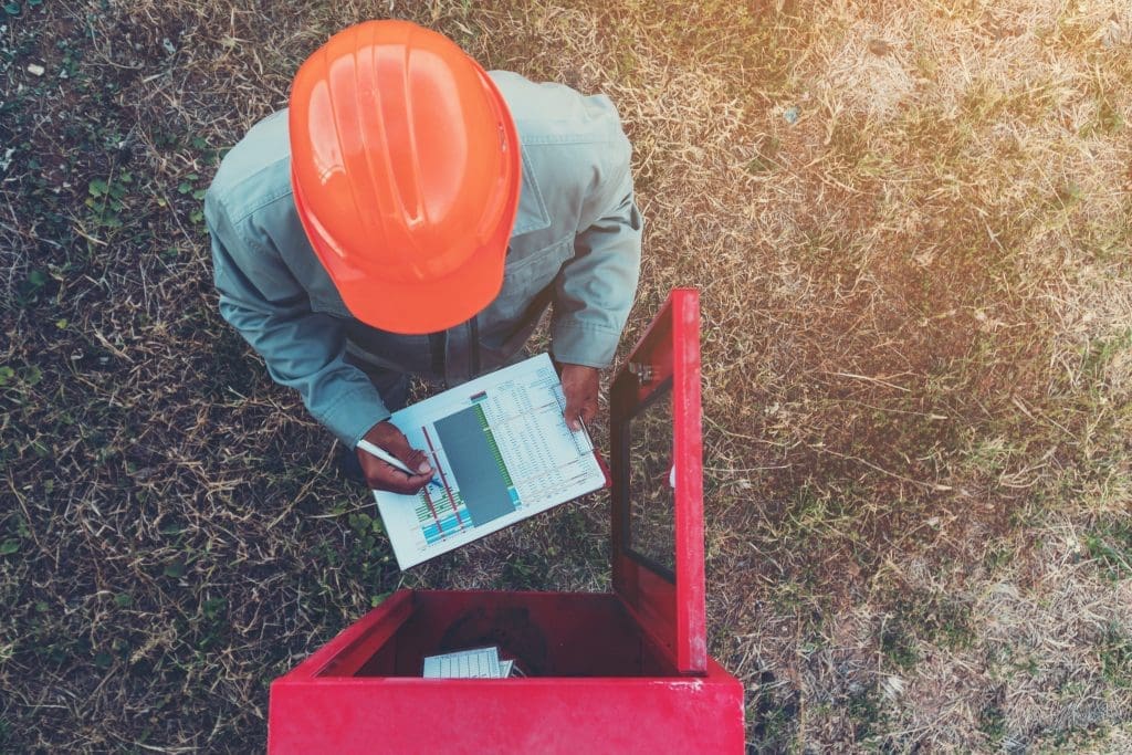 a top down image of a fire sprinkler installer wearing an orange helmet carrying out checks on a piece of equipment.